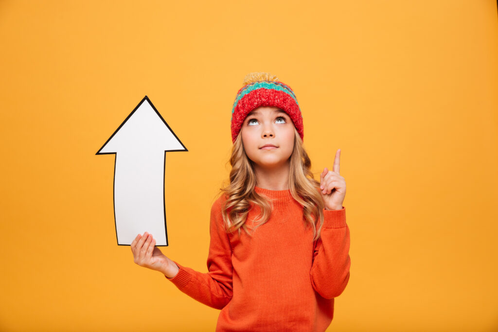 WorldBrain+ young girl sweater hat holding paper arrow while pointing looking up orange